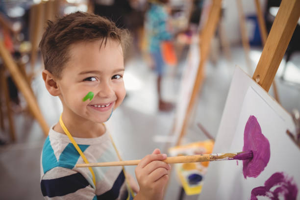 Portrait of happy schoolboy panting on canvas during drawing class