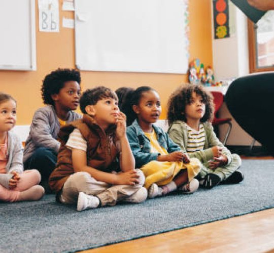 Elementary school students sit and listen to a story from their teacher. Group of young children having a listening comprehension lesson in class. Kids schooling in a multiethnic education centre.