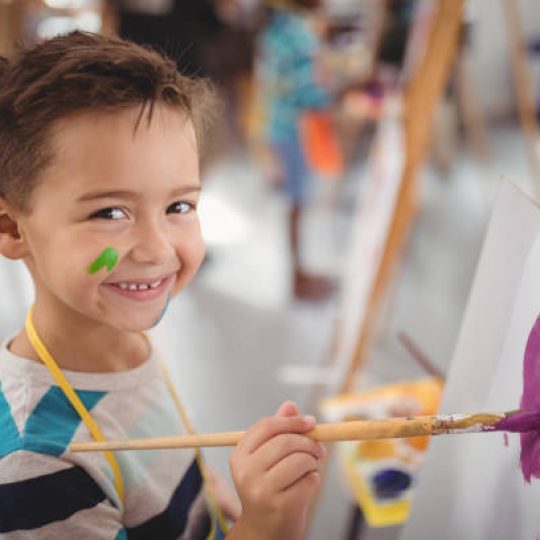 Portrait of happy schoolboy panting on canvas during drawing class